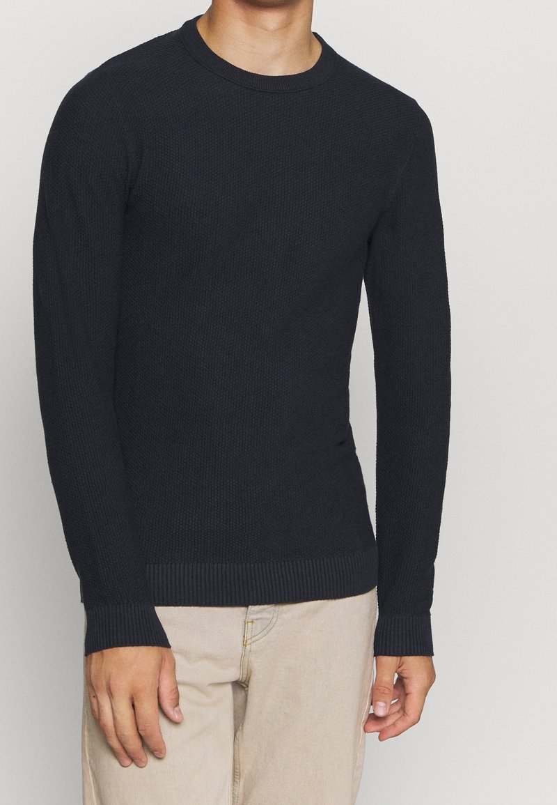 Mörkblå långärmad stickad tröja med ett texturerat mönster, ribbade ärmslut och nederkant. Tillverkad av mjukt material, figursydd vid midjan.