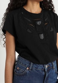 Svart bomullströja med korta ärmar, prydd med en texturerad, präglad tjurdesign framtill. Bärs tillsammans med högmidjade denimjeans.