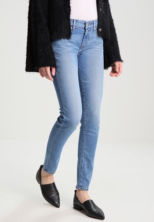 Kobieta nosząca jasnoniebieskie obcisłe dżinsy, czarne buty na niskim obcasie z wąskim noskiem oraz czarny puszysty kardigan na białym topie.