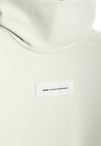 Jersey de cuello alto blanco con una textura suave, que presenta una pequeña etiqueta con la inscripción "MWM x mod wave movement" cosida en el lateral.