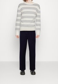 Stripet grå og hvid strikket sweater med en bred crew neckline, parret med mørk navy bukser og sorte chunky sko.