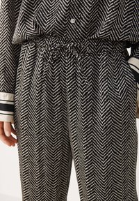 Zwart-wit gestreepte set van shirt en broek in een visgraatpatroon, met een tailleband met trekkoord en contrasterende gestreepte accenten op de manchetten.