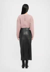 Pulover roz cu croială lejeră, detaliu cu fermoar la spate, combinat cu o fustă maxi din piele neagră cu o cusătură pe mijloc și bocanci până la gleznă.