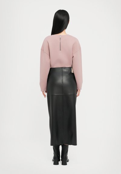 Rosa Pullover mit lockerer Passform, rückseitigem Reißverschluss-Detail, kombiniert mit einem schwarzen Leder-Maxirock, der in der Mitte eine Naht hat, und Ankle Boots.