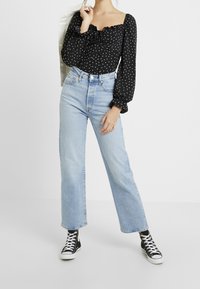 Musta pilkkupaita, jossa on pitkät röyhelösleeves, yhdistettynä korkeavyötäröisiin vaaleansinisiin farkkuihin ja mustiin korkeatoppa-kengiin.