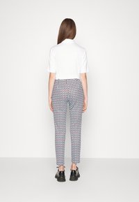 Camisa polo blanca de manga corta, combinada con pantalones multicolores con un diseño geométrico. Unos zapatos negros completan el conjunto.
