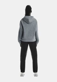 Grauer Kapuzenpullover mit lockerer Passform, kombiniert mit schwarzen Hosen mit seitlichen Reißverschlüssen und weißen Schuhen. Glatte Textur, lässiges Design.