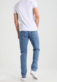 Light blue denim jeans with a straight-leg fit, featuring two back pockets and subtle stitching details, paired with a plain white T-shirt.