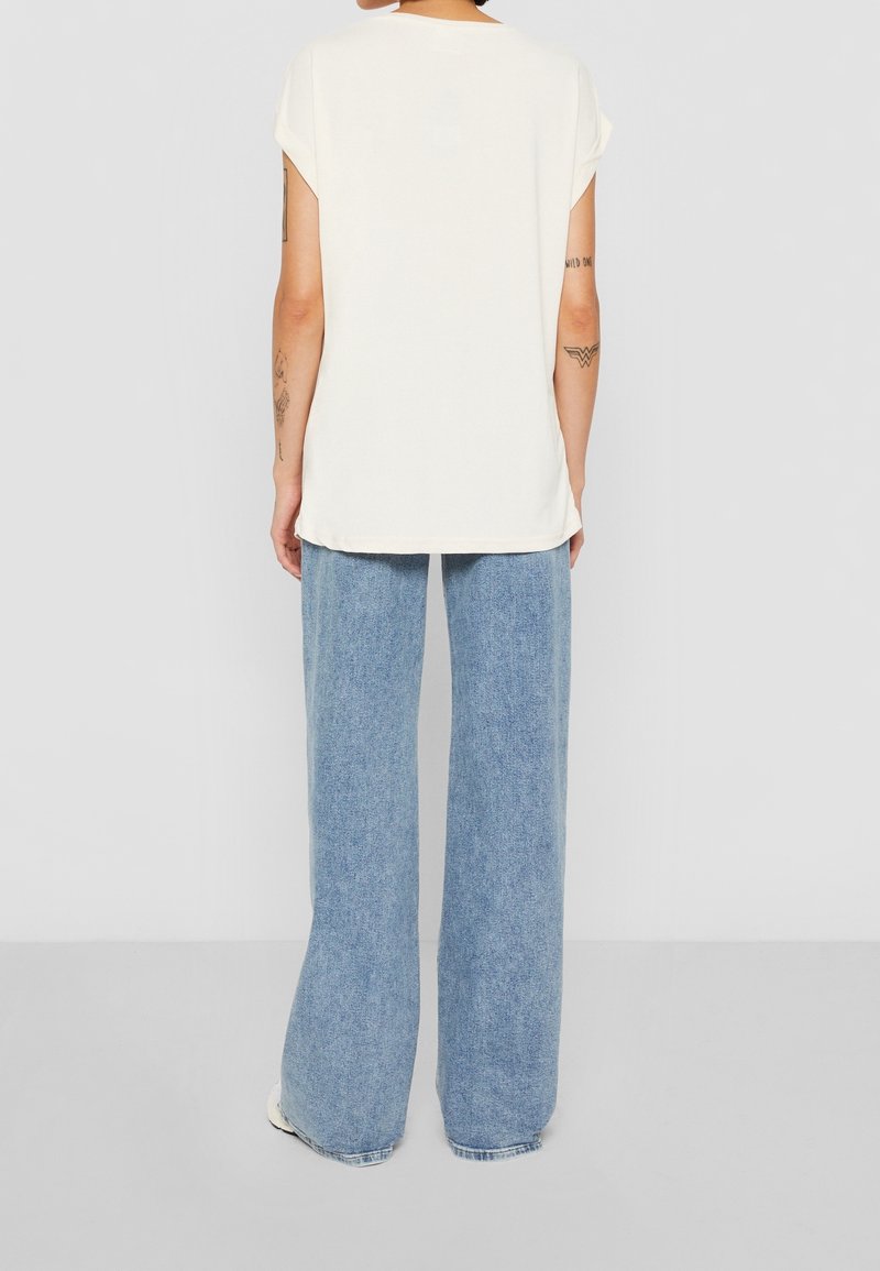 Top corto bianco sporco a maniche corte con una vestibilità ampia, abbinato a jeans a gamba larga di un azzurro chiaro, caratterizzato da un design semplice e da una consistenza morbida.