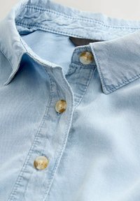 Lichtblauw denim overhemd met een klassieke kraag, voorzien van beige knopen en een zachte textuur. Close-upweergave met focus op de kraag en knopen.