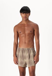 Brown checkered shorts with an elastic waistband, made of lightweight fabric, worn by a shirtless person with straight black hair.