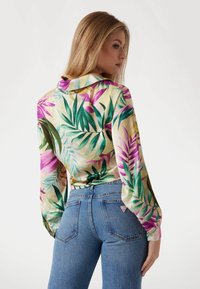 Langd-mouwen blouse met een bloemenpatroon in groen, roze en geel. Gemaakt met hoge taille blauwe jeans, met een driehoekig logo op de achterzak.
