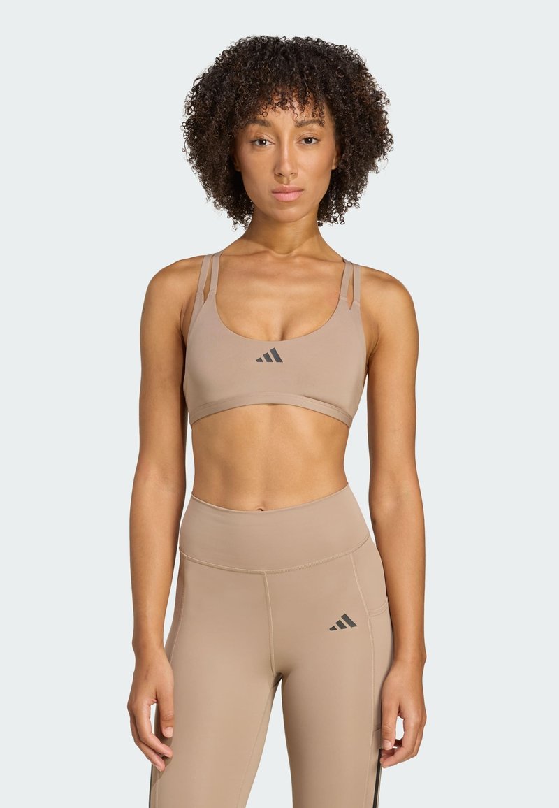 Sujetador deportivo color marrón y leggings de cintura alta, hechos de una tela suave, con tirantes finos y acentos de logotipo negros. Diseño simple y ajustado.