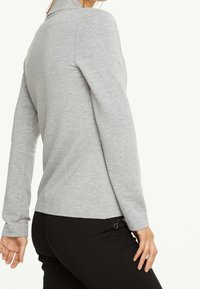 Chemise grise à manches longues avec une texture douce, dotée d'un col polo et d'un ourlet arrondi. Assortie à un pantalon noir avec un détail zip.