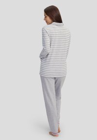 Top de manga larga a rayas grises y blancas con una textura suave, combinado con pantalones lisos grises. Ambos tienen un corte relajado y acentos mínimos.