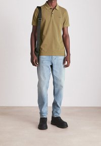 Olivgrön polotröja med krage, lösa ljusblå denimjeans och svarta slipskor. Modellen bär en svart axelväska.