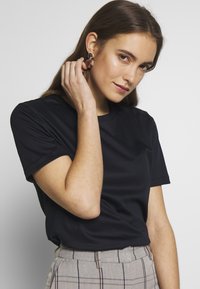 Schwarzes T-Shirt mit kurzen Ärmeln aus glattem Stoff, kombiniert mit hochtaillierten karierten Hosen. Verfügt über einen runden Ausschnitt ohne sichtbare Verzierungen.