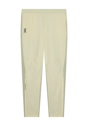 Pantalon de sport beige clair avec taille élastique, petit logo noir sur la cuisse gauche et panneaux de ventilation perforés sur les côtés inférieurs.