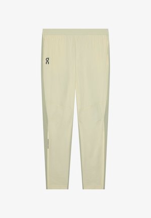 Pantalon de sport beige clair avec taille élastique, petit logo noir sur la cuisse gauche et panneaux de ventilation perforés sur les côtés inférieurs.