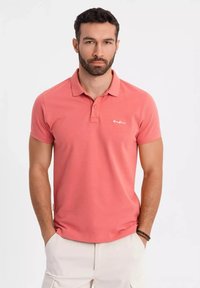 Lyhythihainen korallinvärinen polo paita, jossa on kaksinappinen kaulus, huomaamaton logo-embroidointi rinnassa ja puuvillasekoitekangas.