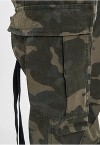 Sötétzöld és bézs árnyalatú kamuflázs cargo nadrág, oldalsó zsebbel, strapabíró anyagból, laza szabással és állítható kötőfűzéssel.