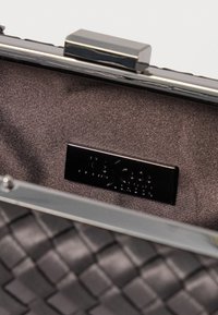 Tamsiai pilkas metalinis užsegimas piniginė su pintu raštu ir satino vidumi. Yra juodas prekės ženklo ženklas. Lygi tekstūra.