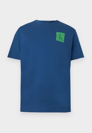 Kék pamut póló kerek nyakkal, rövid ujjakkal és zöld négyzet alakú logóval, amelyen a "cK" design található a bal felső mellen.