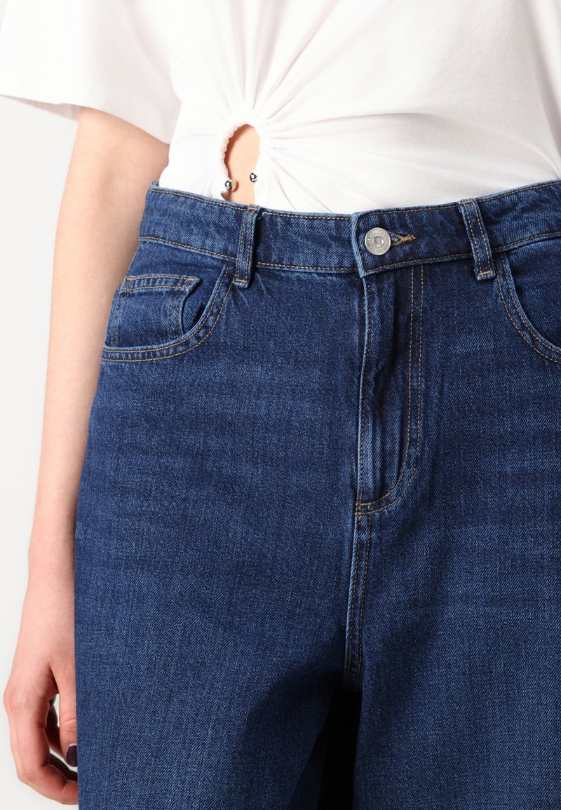 Jeans in denim blu con vita alta, caratterizzati da tasche classiche, chiusura con bottone e un leggero sbiadimento. Tessuto texture con vestibilità strutturata.