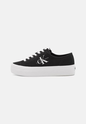 Sorte lærredssneakers med hvid gummiplatformsål, snørebåndsdesign, med et Calvin Klein-logo i hvidt på den laterale side.