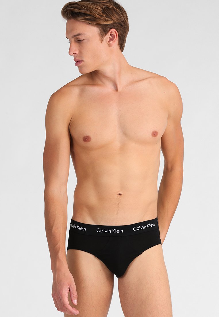 Calzoncillos de algodón negros con una banda suave que presenta la marca 'Calvin Klein' en blanco, ajuste ceñido y textura suave. Modelo de perfil derecho, sin camiseta.