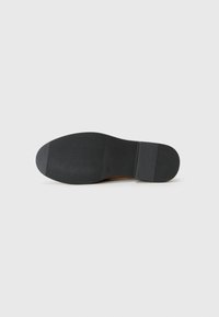 Semelle de chaussure en caoutchouc noir avec des motifs de texture pour une meilleure adhérence sur un fond gris clair. Le talon présente une légère courbure pour le confort.