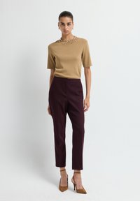 Haut brun à manches courtes avec un col orné de perles, associé à un pantalon bordeaux et des chaussures à talons hauts marron. Tissu lisse, design ajusté.