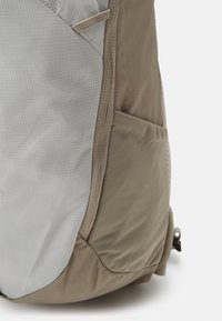 Beige és szürke nylon hátizsák, amely texturált felülettel, oldalsó zsebbel és megerősített varratokkal rendelkezik a tartósság érdekében.