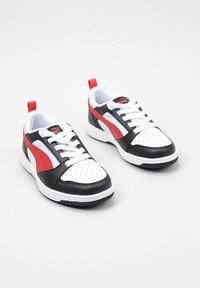 Sneaker bianco e nero con accenti rossi, punta perforata, stringhe bianche e colletto imbottito. Presenta una suola testurizzata per una buona aderenza.