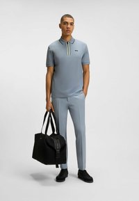 Jasnoszary golf z kołnierzem polo i trójkolorowym paskiem. W połączeniu z dopasowanymi spodniami i czarną torbą podróżną. Czarne sportowe buty.