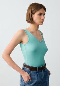 Un body a coste verde menta con scollo a V, abbinato a pantaloni corti di jeans blu a vita alta e una cintura marrone.