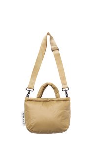 Beige padded bag with dual handles and adjustable strap. Features a smooth texture and brand label on the side. Compact rectangular shape.