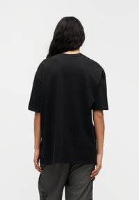 Μαύρο φαρδύ T-shirt με κοντά μανίκια, στρογγυλή λαιμόκοψη και λείο ύφασμα, φορεμένο πάνω από σκούρα παντελόνια cargo.