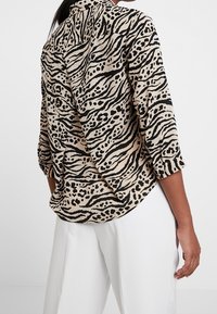 Béžová halenka s černým vzorem tygřích pruhů, kulatým výstřihem a tříčtvrtečními rukávy. Měkká tkanina s volným střihem.