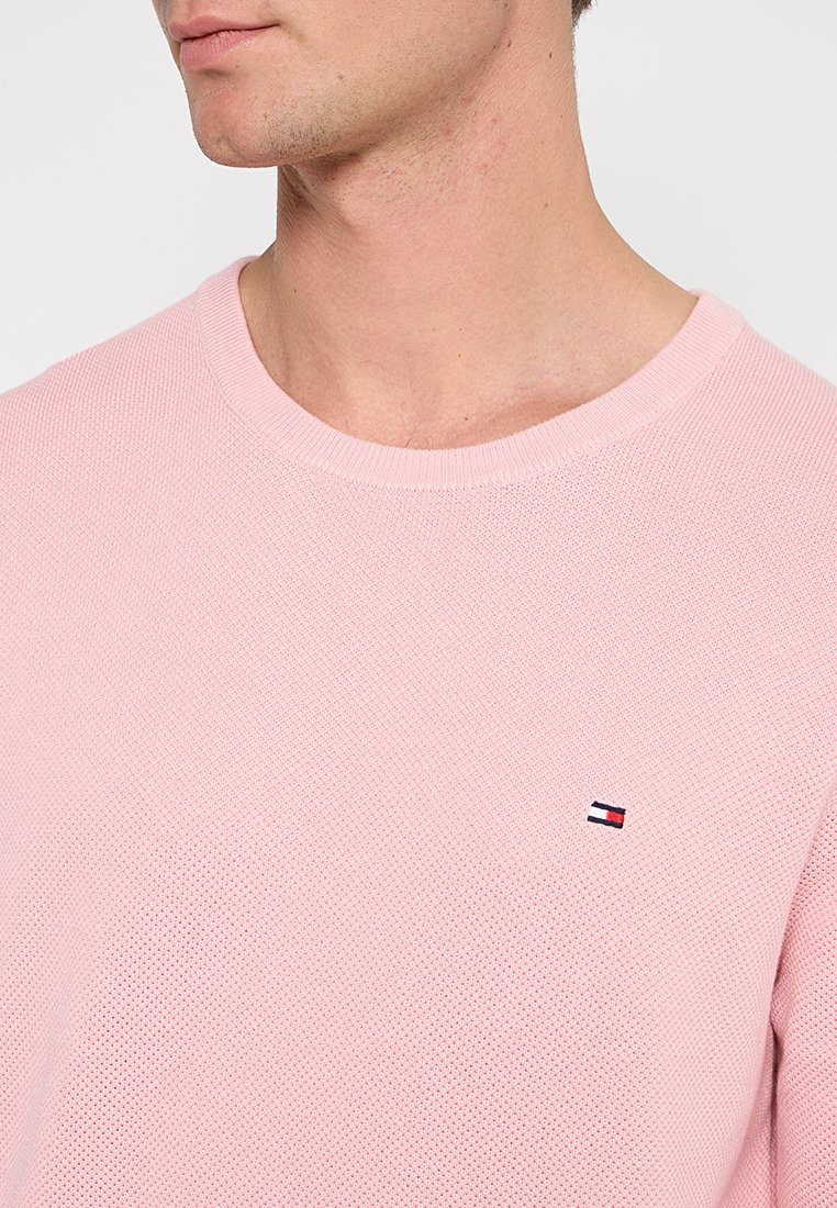 Hellrosa Strickpullover mit Rundhalsausschnitt, ausgestattet mit einem kleinen, gestickten Logo auf der linken Brust. Strukturiertes, atmungsaktives Material.