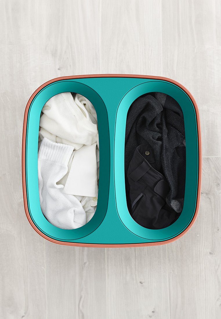 Zweifächer-Wäschekorb in Türkis mit einem Kupferakzent. Beinhaltet weiße Socken und ein Hemd auf der einen Seite, schwarze Kleidung auf der anderen.