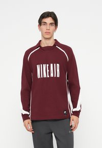 Sweatshirt granada com riscas brancas nas laterais, apresenta um colarinho dobrado e um gráfico "NIKE AIR" na parte da frente, feito de tecido suave.