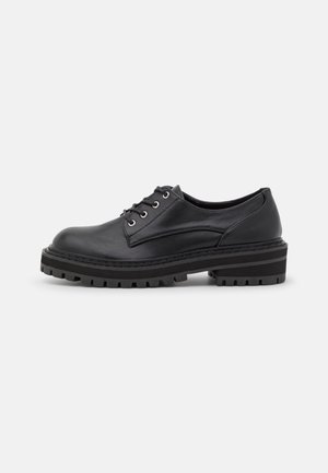 Chaussure oxford en cuir noir avec bout rond, lacets à l'avant et semelle en caoutchouc épaisse dotée d'un motif de bande de roulement texturé. Surface lisse et design minimaliste.