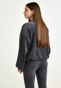 Grå velour sweatshirt med en afslappet pasform, drop-skuldrer og ribbede manchetter, parret med matchende velourbukser. Blød tekstur og minimalistisk design.