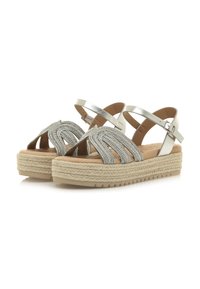 Sandales à brides torsadées argentées avec une plateforme beige, accent en jute tressé et bride de cheville réglable. Semelle intérieure texturée pour le confort.