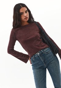 Burgunderfarbenes Langarmshirt mit rundem Halsausschnitt und verblasster Textur, kombiniert mit blauen Jeans und einer schwarzen Handtasche.