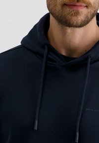 Marineblaue Kapuzenjacke mit Kordelzugkapuze, weichem Stoff, gerippten Bündchen und einem Logo-Textdetail auf der Vorderseite. Glattes, lässiges Design.