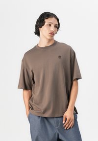Brown cotton t-shirt with a loose fit, crew neckline, and short sleeves. Features a small, embossed logo on the upper left chest.
