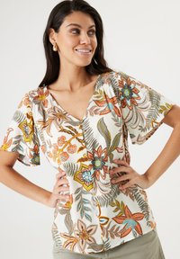 Blusa floral de manga corta, con cuello en V y detalle de botones. Presenta patrones coloridos en naranja, azul y verde sobre un fondo crema.