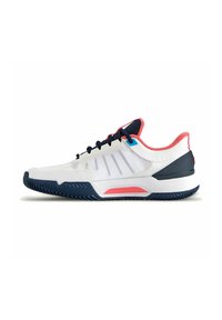 Zapatilla deportiva blanca con acentos en azul marino y rojo, parte superior de malla, suela texturizada y media suela acolchada. Los cordones y las franjas laterales son características destacadas.